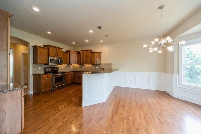 1420 Hannah Ln, Waukee, IA 50263 - kitchen with stainless steel appliances, brown cabinetry, wood finished floors, dark stone countertops, and arched walkways