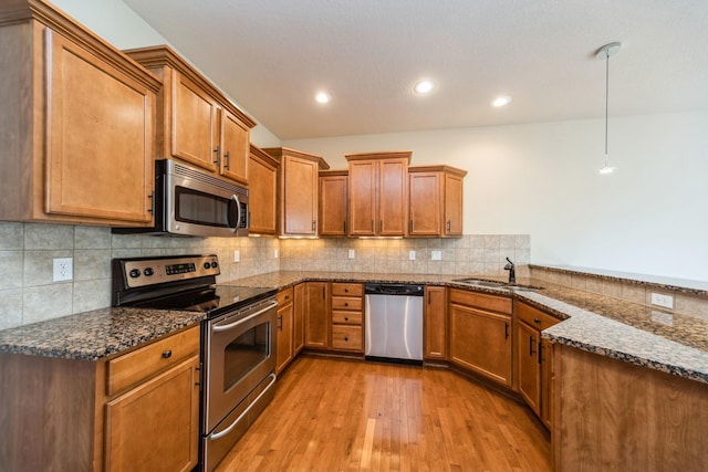 1420 Hannah Ln, Waukee, IA 50263 - kitchen with appliances with stainless steel finishes, light wood-type flooring, brown cabinets, dark stone counters, and recessed lighting