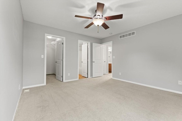 unfurnished bedroom featuring a walk in closet, light colored carpet, baseboards, connected bathroom, and a closet