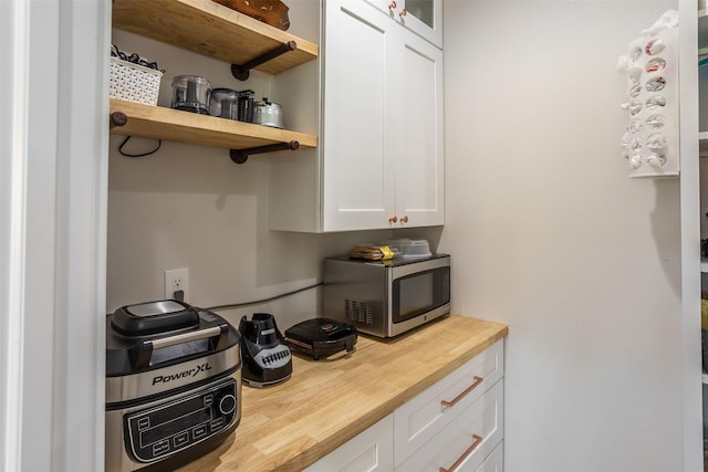 2770 NW 167th St, Clive, IA 50325 - kitchen with stainless steel microwave, wood counters, white cabinetry, open shelves, and glass insert cabinets