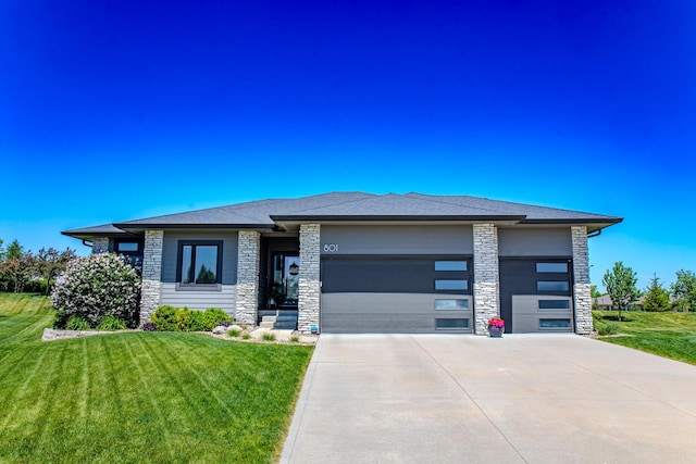 prairie-style house featuring an attached garage, stone siding, driveway, and a front lawn