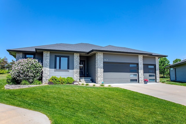 prairie-style home featuring stone siding, an attached garage, driveway, and a front lawn