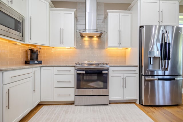 kitchen with stainless steel appliances, wall chimney range hood, light wood finished floors, and white cabinetry