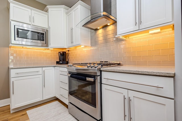 kitchen with appliances with stainless steel finishes, wall chimney range hood, white cabinets, and backsplash
