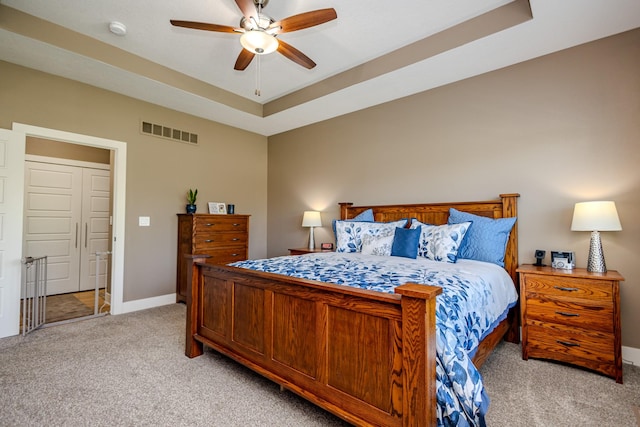 bedroom featuring light colored carpet, baseboards, ceiling fan, and a tray ceiling