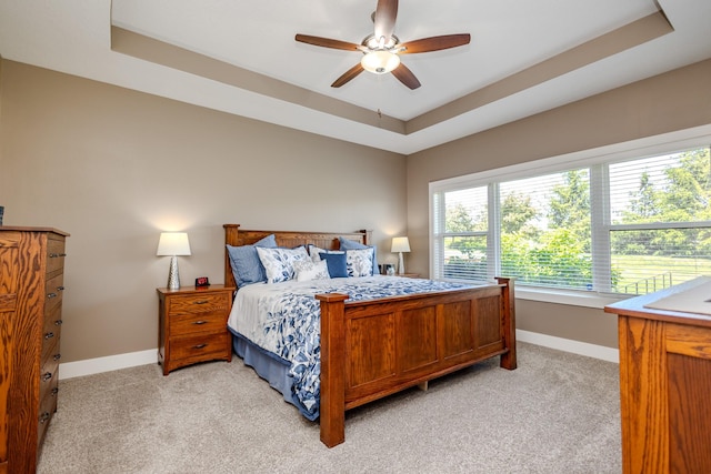 bedroom with a raised ceiling, light carpet, baseboards, and ceiling fan