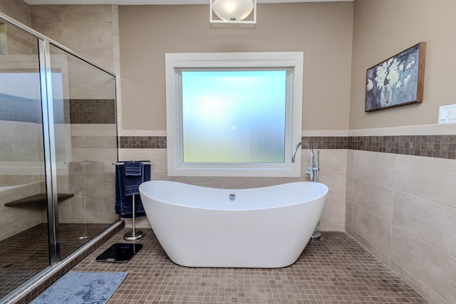 bathroom with tile walls, tile patterned floors, a stall shower, a freestanding bath, and wainscoting
