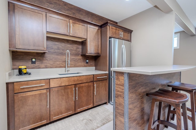 kitchen featuring a sink, freestanding refrigerator, a kitchen breakfast bar, and light countertops