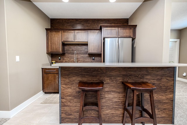 kitchen featuring freestanding refrigerator, baseboards, a breakfast bar area, and dark brown cabinetry