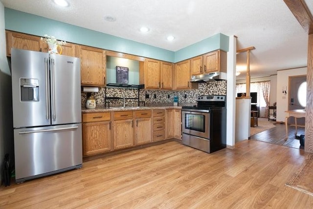 2002 12th St, Eldora, IA 50627 - kitchen with stainless steel appliances, under cabinet range hood, a sink, decorative backsplash, and light wood-style floors