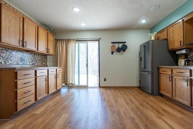 2002 12th St, Eldora, IA 50627 - kitchen featuring a textured ceiling, light wood-style floors, tasteful backsplash, brown cabinetry, and high end fridge