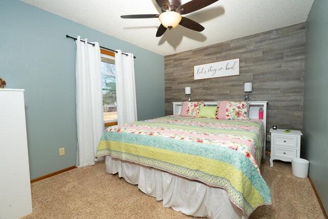 2002 12th St, Eldora, IA 50627 - carpeted bedroom featuring an accent wall, wood walls, a ceiling fan, and baseboards