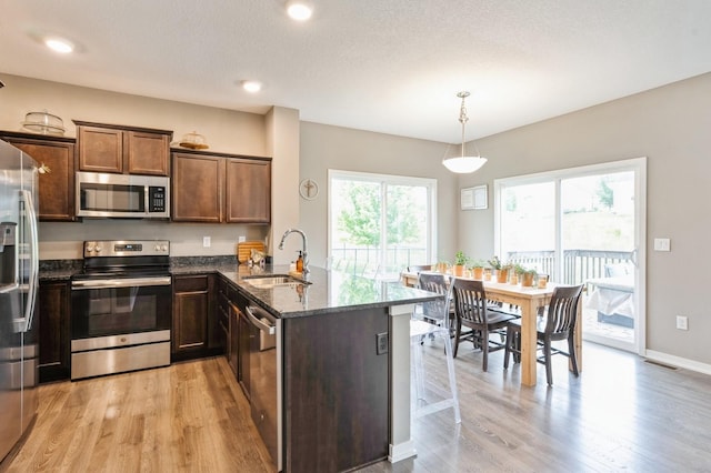 1085 Juniper Dr, Carlisle, IA 50047 - kitchen featuring appliances with stainless steel finishes, a sink, a peninsula, dark stone countertops, and light wood finished floors