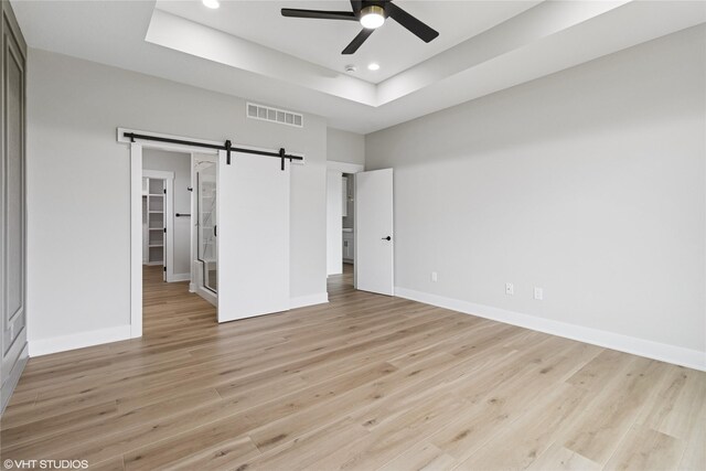 17400 Springbrook Trl, Urbandale, IA 50111 - unfurnished bedroom with a tray ceiling, recessed lighting, a barn door, light wood-style flooring, and baseboards
