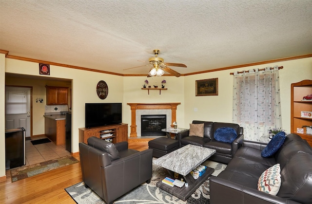 1236 63rd St, Windsor Heights, IA 50324 - living area featuring light wood finished floors, a ceiling fan, crown molding, a tiled fireplace, and a textured ceiling