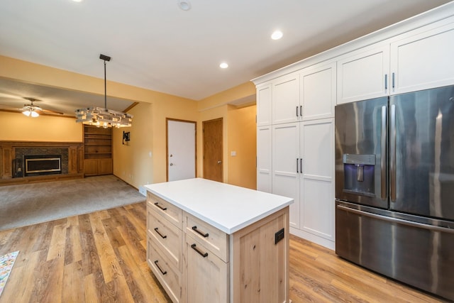 2230 NW 138th St, Clive, IA 50325 - kitchen featuring stainless steel refrigerator with ice dispenser, a kitchen island, ceiling fan, white cabinets, and a fireplace with raised hearth