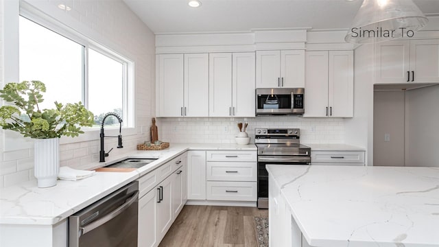 610 NW Georgetown Dr, Waukee, IA 50263 - kitchen featuring stainless steel appliances, a sink, white cabinets, light wood finished floors, and tasteful backsplash