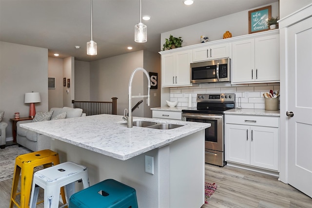 1917 Southbridge Dr, Adel, IA 50003 - kitchen featuring appliances with stainless steel finishes, backsplash, light wood-type flooring, white cabinets, and a breakfast bar