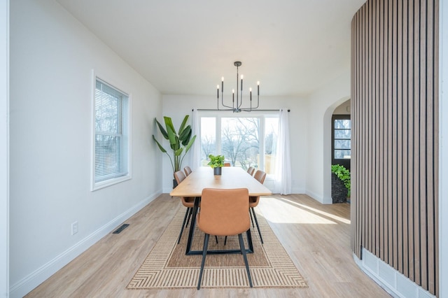 211 Park Ave, Des Moines, IA 50315 - dining room with arched walkways, light wood-style flooring, a chandelier, and baseboards