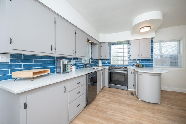 211 Park Ave, Des Moines, IA 50315 - kitchen featuring stainless steel appliances, a sink, light wood-style floors, tasteful backsplash, and light countertops