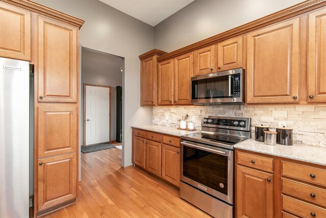 3605 151st St, Urbandale, IA 50323 - kitchen with stainless steel appliances, decorative backsplash, light wood-style floors, light stone countertops, and brown cabinets