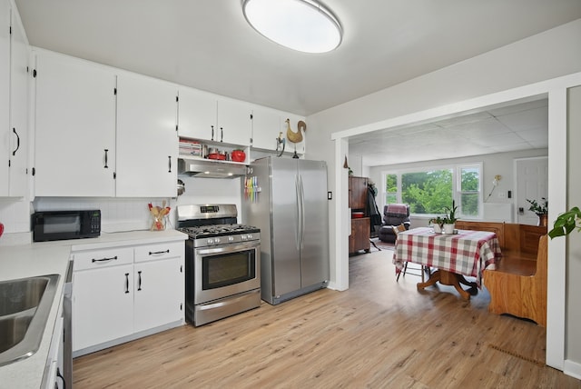 819 Olinda Ave, Des Moines, IA 50315 - kitchen featuring stainless steel appliances, light wood finished floors, under cabinet range hood, white cabinets, and backsplash
