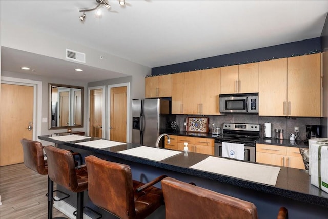 400 Walnut St Unit 803, Des Moines, IA 50309 - kitchen featuring appliances with stainless steel finishes, a breakfast bar area, tasteful backsplash, light brown cabinetry, and dark countertops