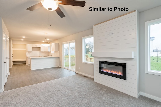 25087 Bluebird Cir, Adel, IA 50003 - unfurnished living room with baseboards, a glass covered fireplace, ceiling fan, and light carpet
