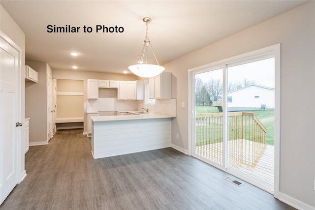 25087 Bluebird Cir, Adel, IA 50003 - kitchen with wood finished floors, a peninsula, baseboards, white cabinetry, and decorative light fixtures
