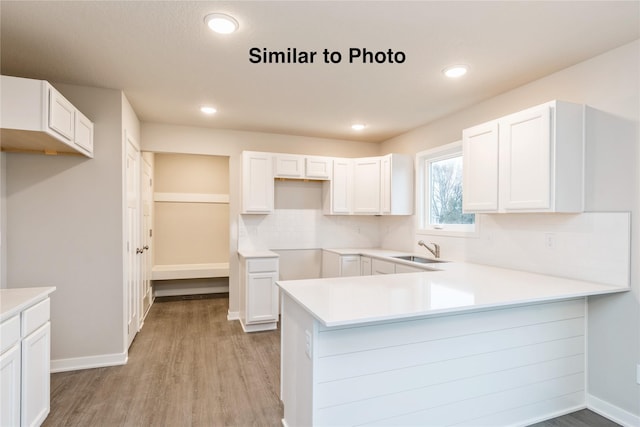 25087 Bluebird Cir, Adel, IA 50003 - kitchen with a peninsula, light wood-style flooring, white cabinets, a sink, and tasteful backsplash