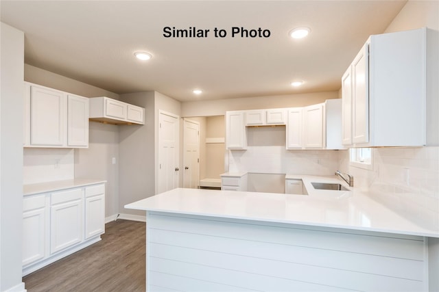 25087 Bluebird Cir, Adel, IA 50003 - kitchen featuring a sink, a peninsula, wood finished floors, tasteful backsplash, and white cabinetry