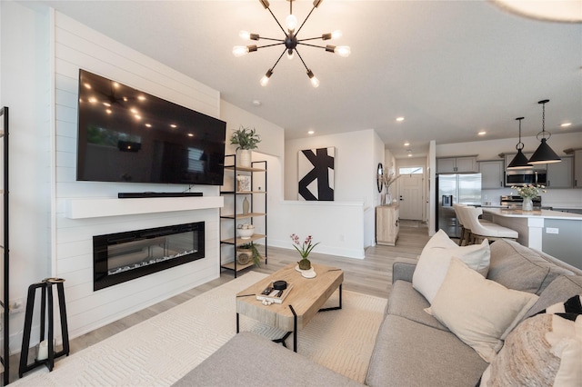 523 NE Vista Ln, Ankeny, IA 50021 - living area with light wood-style floors, a chandelier, a glass covered fireplace, recessed lighting, and baseboards