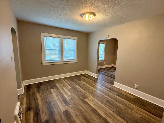3916 Cambridge St, Des Moines, IA 50313 - empty room with arched walkways, a textured ceiling, dark wood-type flooring, and baseboards