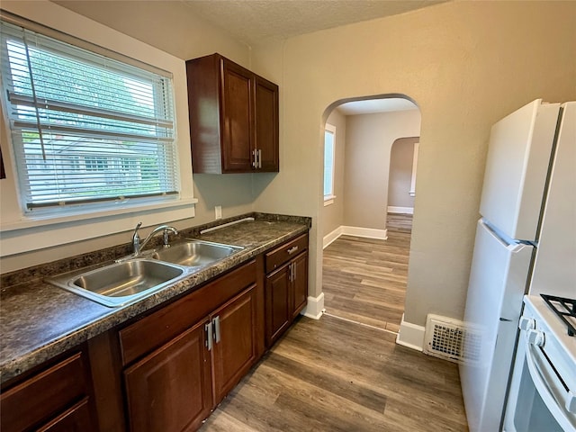 3916 Cambridge St, Des Moines, IA 50313 - kitchen with white appliances, a sink, dark countertops, wood finished floors, and arched walkways