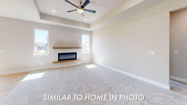 2540 E 50th Ct, Des Moines, IA 50317 - unfurnished living room featuring a glass covered fireplace, ceiling fan, baseboards, a raised ceiling, and carpet flooring