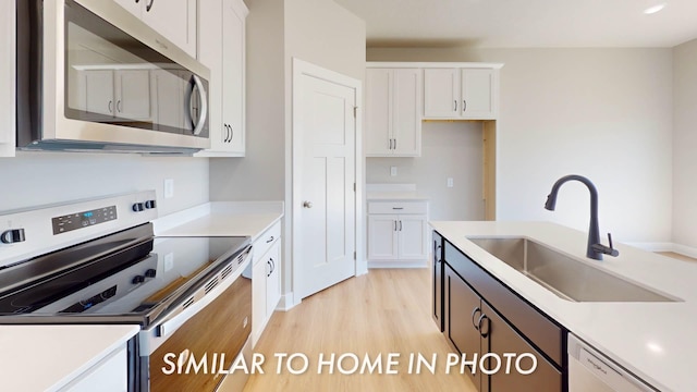 2540 E 50th Ct, Des Moines, IA 50317 - kitchen featuring stainless steel appliances, a sink, white cabinetry, light wood-style flooring, and light countertops