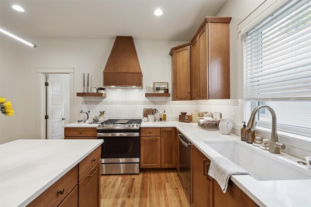 1107 24th St, Des Moines, IA 50311 - kitchen featuring appliances with stainless steel finishes, custom exhaust hood, a sink, brown cabinets, and light wood-type flooring