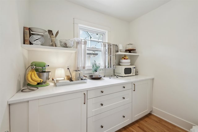 1107 24th St, Des Moines, IA 50311 - bar featuring white microwave, light wood-style floors, and baseboards