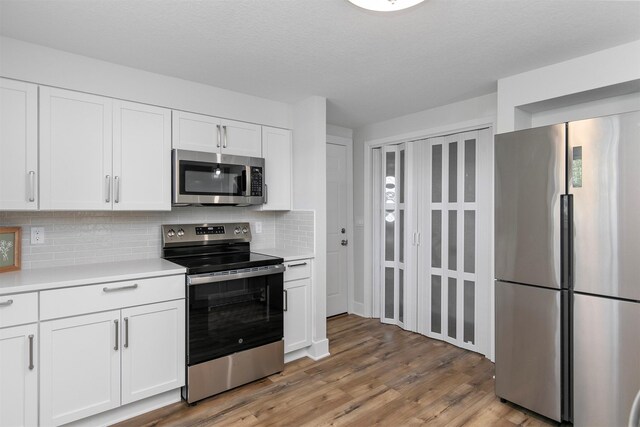 205 NW 51st Pl, Des Moines, IA 50313 - kitchen with appliances with stainless steel finishes, light countertops, backsplash, white cabinets, and light wood-style floors