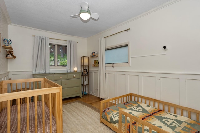 2740 Forest Dr, Des Moines, IA 50312 - bedroom with light wood-style floors, a decorative wall, crown molding, wainscoting, and a crib