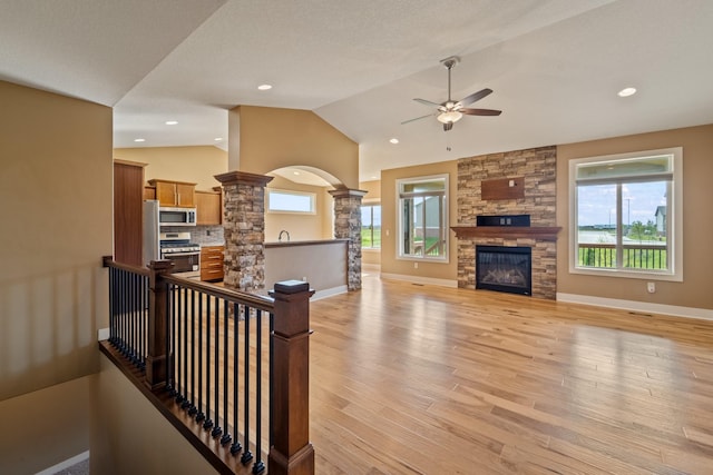 916 NE Silkwood St, Grimes, IA 50111 - living room featuring a ceiling fan, a stone fireplace, vaulted ceiling, decorative columns, and light wood finished floors