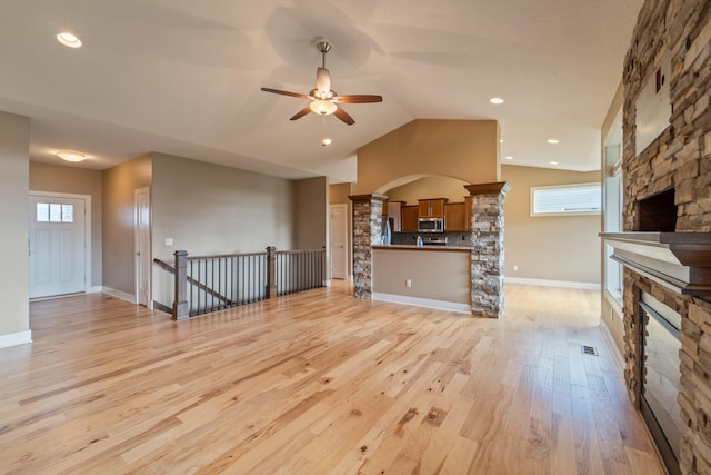 916 NE Silkwood St, Grimes, IA 50111 - unfurnished living room featuring a stone fireplace, ceiling fan, arched walkways, light wood-style floors, and ornate columns