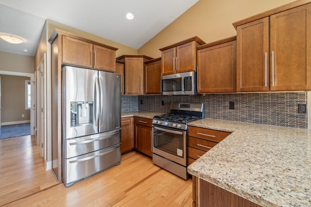 916 NE Silkwood St, Grimes, IA 50111 - kitchen with appliances with stainless steel finishes, brown cabinetry, vaulted ceiling, light wood-type flooring, and backsplash