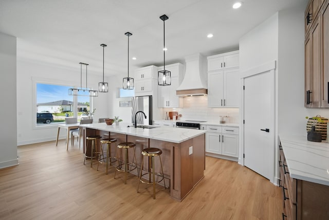 16332 Northpark Dr, Urbandale, IA 50323 - kitchen with custom range hood, light wood-style floors, a sink, a kitchen breakfast bar, and decorative backsplash