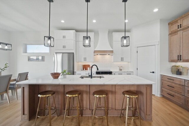 16332 Northpark Dr, Urbandale, IA 50323 - kitchen with freestanding refrigerator, wall chimney range hood, a sink, light wood finished floors, and decorative backsplash