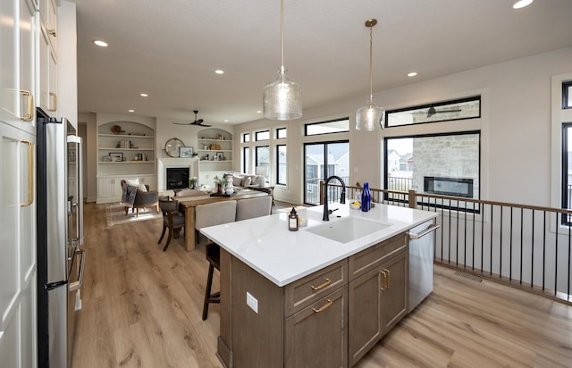 6204 Aspen Dr, West Des Moines, IA 50266 - kitchen featuring a glass covered fireplace, a sink, light wood-style floors, appliances with stainless steel finishes, and a kitchen island with sink