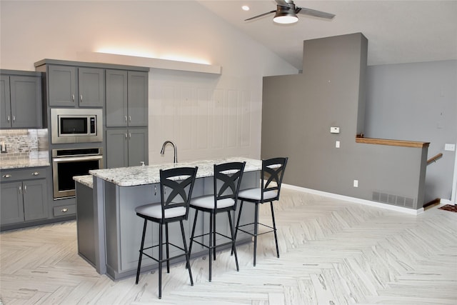 730 Kitterman Cir, Norwalk, IA 50211 - kitchen featuring appliances with stainless steel finishes, gray cabinets, light stone counters, ceiling fan, and a kitchen bar
