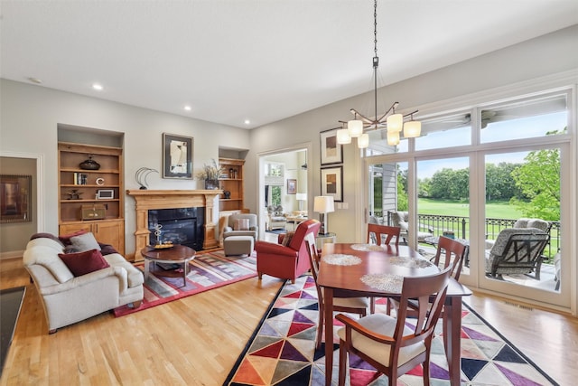 1176 Glen Oaks Dr, West Des Moines, IA 50266 - dining room with wood finished floors, a chandelier, a glass covered fireplace, built in features, and recessed lighting