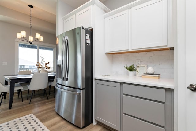 3309 NW Reinhart Dr, Ankeny, IA 50023 - kitchen with stainless steel fridge with ice dispenser, a chandelier, decorative backsplash, light countertops, and light wood finished floors