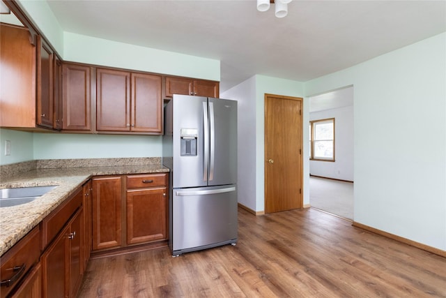 221 W Division St, Colfax, IA 50054 - kitchen with stainless steel refrigerator with ice dispenser, light wood-style flooring, baseboards, light stone countertops, and brown cabinets
